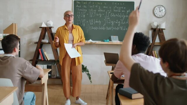 Zoom in of female teacher explaining math formulas on chalkboard to diverse students during college lesson in classroom