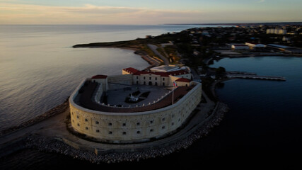 Old castle on a narrow isthmus in the sea channel. Dark water and gray defensive ancient structure in the rays of the setting sun.