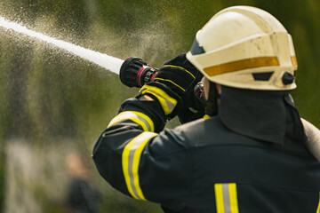 One young male firefighter on duty dressed in uniform with water hose extinguishing fire