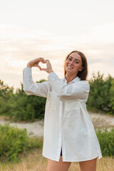 Fototapeta na wymiar Female making heart shape hand on a garden at sunset. Woman in nature holding heart shape.Love and nature beauty concept