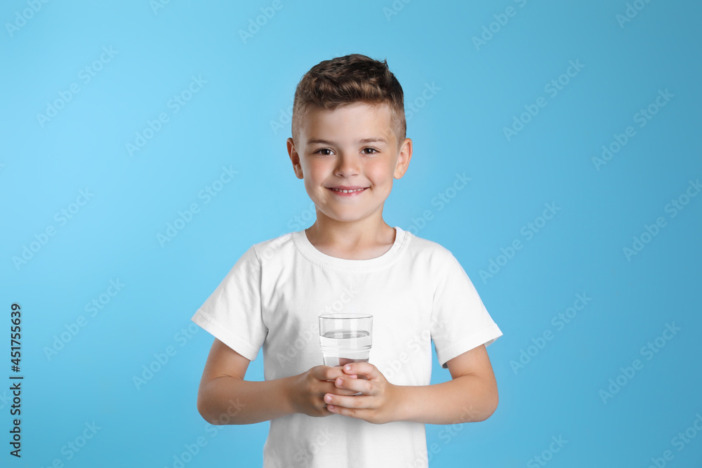 Poster Cute little boy with glass of water on light blue background