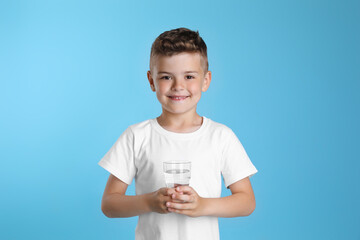 Cute little boy with glass of water on light blue background