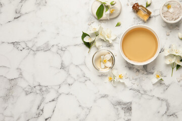 Flat lay composition with jasmine essential oil and fresh flowers on white marble table. Space for text