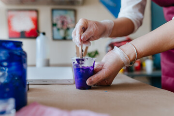 Female artist pouring acrylic medium for painting picture in fluid pouring technique