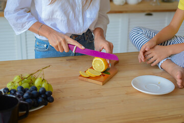 Close-up woman hands cut lemon with sharp knife in kitchen