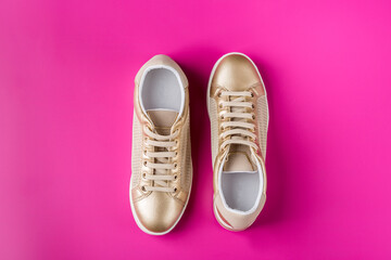 Pair of golden female sneakers on pink background