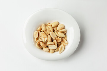 Roasted salted peanuts in a white plate. Appetizing snack. Close-up. White background.