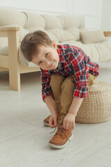 Cute little boy tying shoe laces at home
