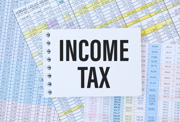 Income Tax text on paper sheet on chart on wooden table - business, banking, finance and investment concept