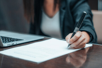 Mujer joven firma en un papel un contrato de trabajo junto a su ordenador