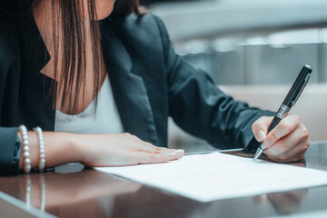 Mujer joven firma en un papel un contrato de trabajo junto a su ordenador