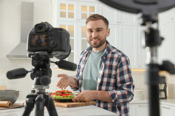 Blogger with tasty croissant recording video in kitchen at home. Using ring lamp and camera