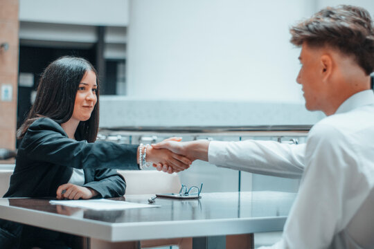 Muchacha joven realiza un apreton de manos en la mesa con su cliente en su oficina