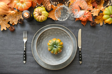 Thanksgiving day table setting with pumpins and grey plate decorated autumn leaves, candle and cozy garland on gray linen tablecloth. Top view.