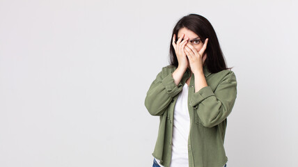 pretty woman feeling scared or embarrassed, peeking or spying with eyes half-covered with hands