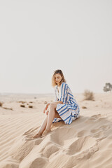Fototapeta na wymiar Young woman in blue dress sitting on a sand dune in a wild desert