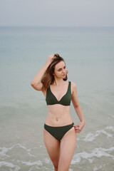 Young woman wearing khaki bikini standing at the beach near water. Travel and vacation