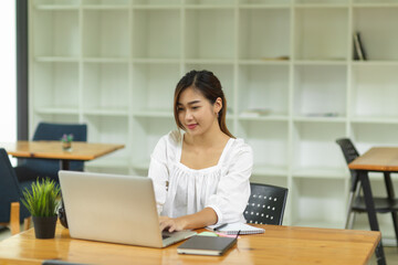 Fototapeta na wymiar Elegant female college student sitting and using laptop computer in library
