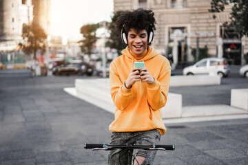 Young african boy with bike listening music with headphones outdoors - Focus on face