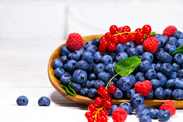 Blueberry, Red Currant and Raspberry With a Green Mint leaf in a Wooden Bowl on a white top view, Summer Freshly Berry, Copyspace