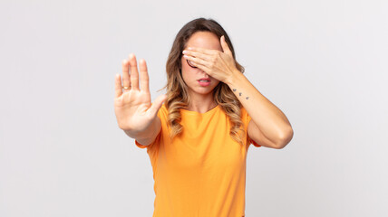 pretty thin woman covering face with hand and putting other hand up front to stop camera, refusing...
