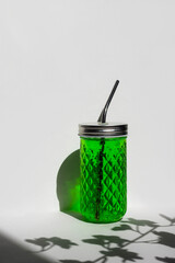 Transparent glass of with green lemonade with reusable metal eco straw in sunlight with shadow.