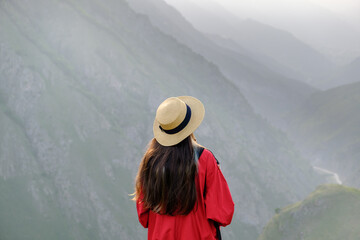 Fototapeta na wymiar Young girl with long hair and a hat enjoying a beautiful mountain landscape Wanderlust and travel concept. Hiking journey on tourist trail