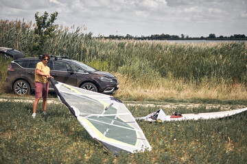 Windsurfer and camper packing and unpacking from a car's roof rack in nature.