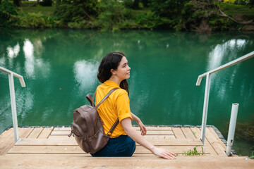 Psychology concept. Woman is sitting on the pier and turn around. The water surface of a green...