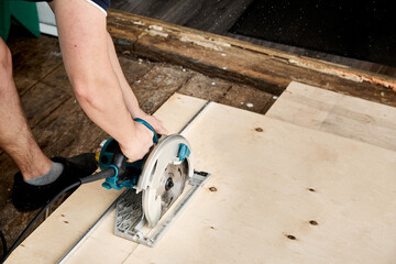 Sawing plywood by circular saw. Home repair. Hand tool. Man hold equipment. Building process. Woodworking. Safety engineering. Without gloves. Copy space. Indoor. Cutting material. Rental instrument