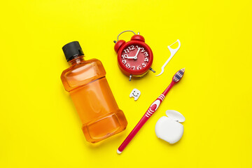 Mouthwash, toothbrush, dental floss and alarm clock on yellow background, flat lay