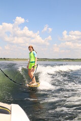 A girl is learning to ride a wakesurf on the lake behind a boat. Newcomer. Training. Wake vest