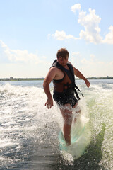 A man is learning to ride a wakesurf on the lake behind a boat. Newcomer. Training. Wake vest