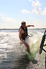A man is learning to ride a wakesurf on the lake behind a boat. Newcomer. Training. Wake vest