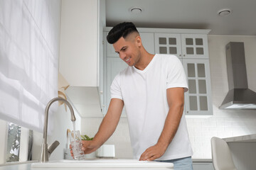 Man filling glass with water from tap in kitchen