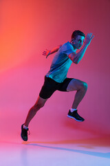 Fototapeta na wymiar Portrat of Caucasian professional male athlete, runner training isolated on pink studio background with blue neon filter, light. Muscular, sportive man.