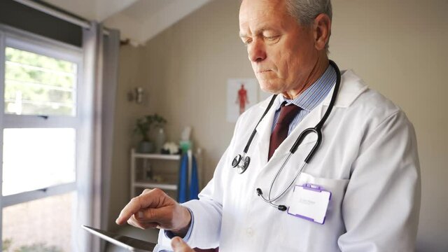 Caucasian male doctor swiping on digital tablet submitted test results of patient, standing in clinic.
