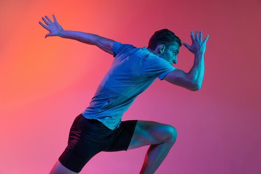 Portrat of Caucasian professional male athlete, runner training isolated on pink studio background with blue neon filter, light. Muscular, sportive man. Back view