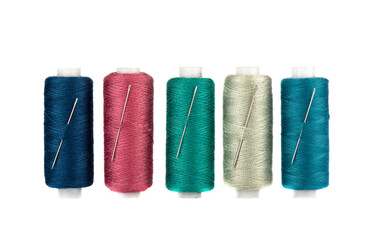 Row of spools of thread of different colors and sewing needles inserted into the spools.
