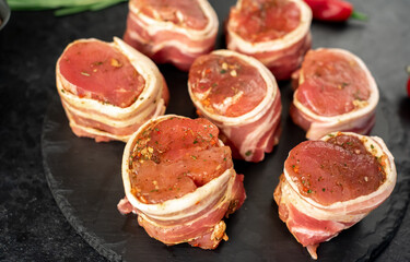raw pork tenderloin medallions wrapped in bacon on a stone background