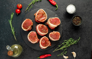 raw pork tenderloin medallions wrapped in bacon on a stone background