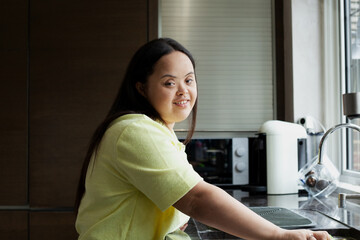 Fototapeta na wymiar Young biracial woman with Down Syndrome cleaning the kitchen and smiling