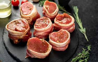 raw pork tenderloin medallions wrapped in bacon on a stone background