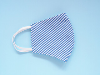 Top view, Fabric face mask blue-white stripes to prevention pollution and viruses. DIY handmade from cotton muslin on blue background. Healthcare, Medical and New normal concept. Copy space.