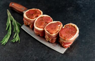 raw pork tenderloin medallions wrapped in bacon on a stone background	