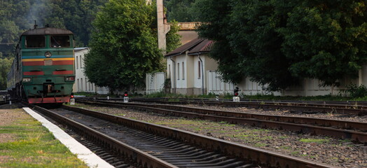 A diesel locomotive with wagons passes near the station