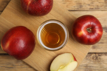 Glass of delicious cider and ripe red apples on wooden table, flat lay
