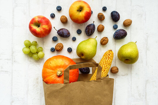 Obst, Gem&uuml;se und N&uuml;sse in einer Papier Einkaufstasche und auf einem wei&szlig;en isolierten Hintergrund verstreut. Draufsicht, Herbst Hintergrund.
