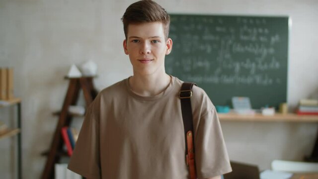 Portrait of young handsome male student with backpack posing for camera in classroom