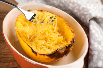 Half of cooked spaghetti squash and fork in baking dish on table, closeup